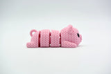 Close-up of a knitted pig keychain with crochet texture and small black eyes, shown against a white background