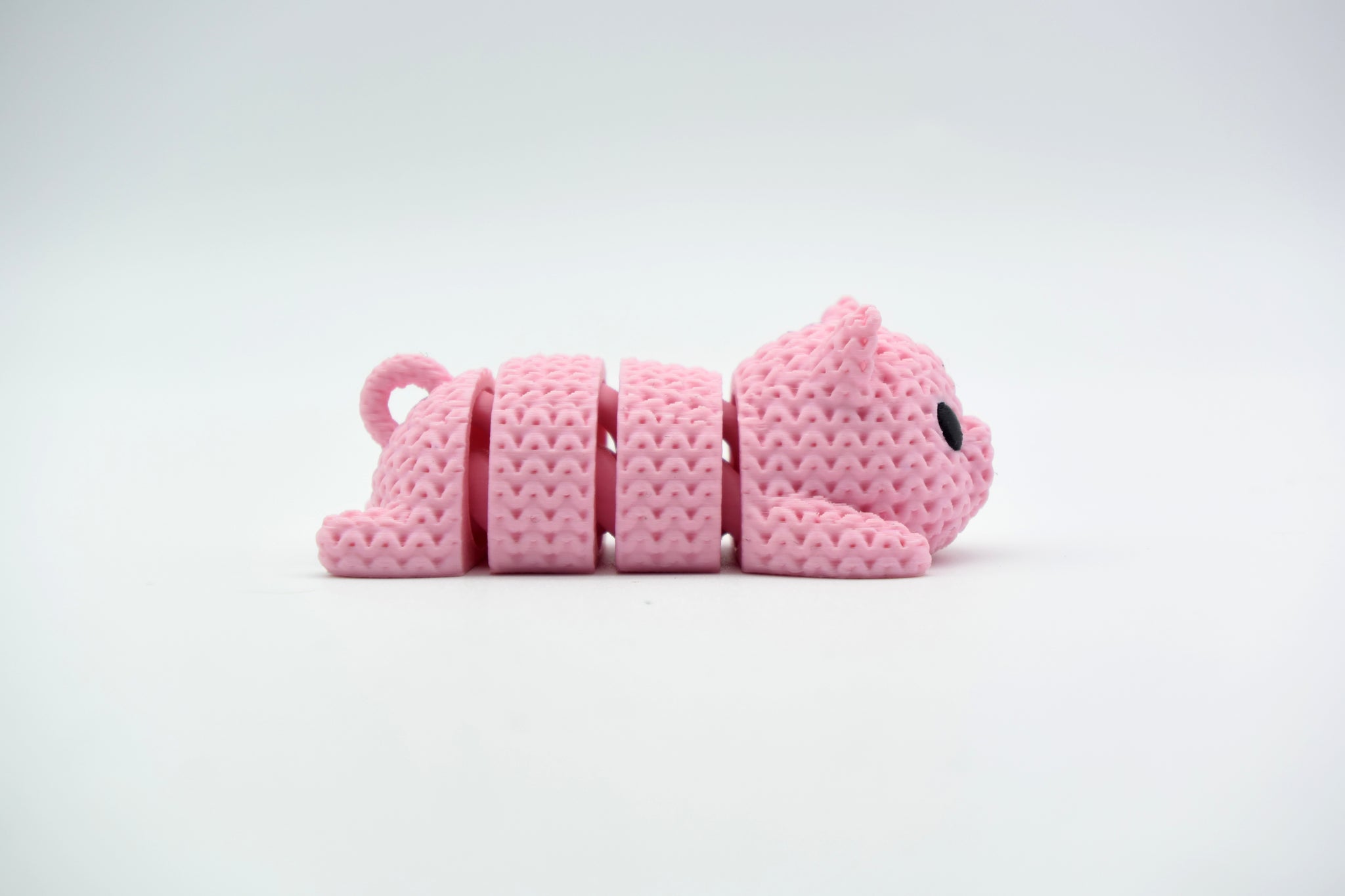 Close-up of a knitted pig keychain with crochet texture and small black eyes, shown against a white background