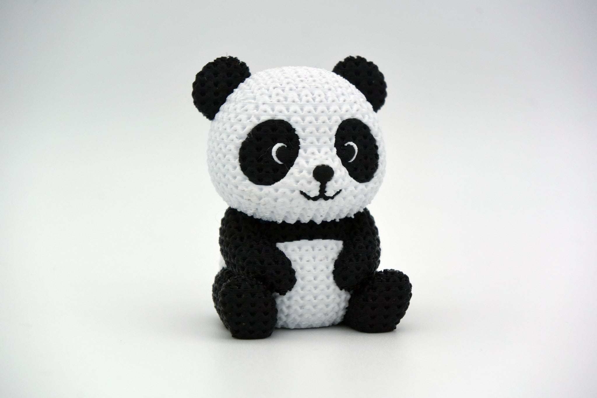 Knitted panda figure styled on a wooden shelf next to plants and neutral home decor