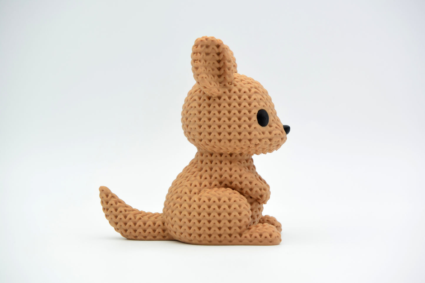 Knitted kangaroo decorative figure standing on a wooden shelf beside small plants and Scandinavian home accessories
