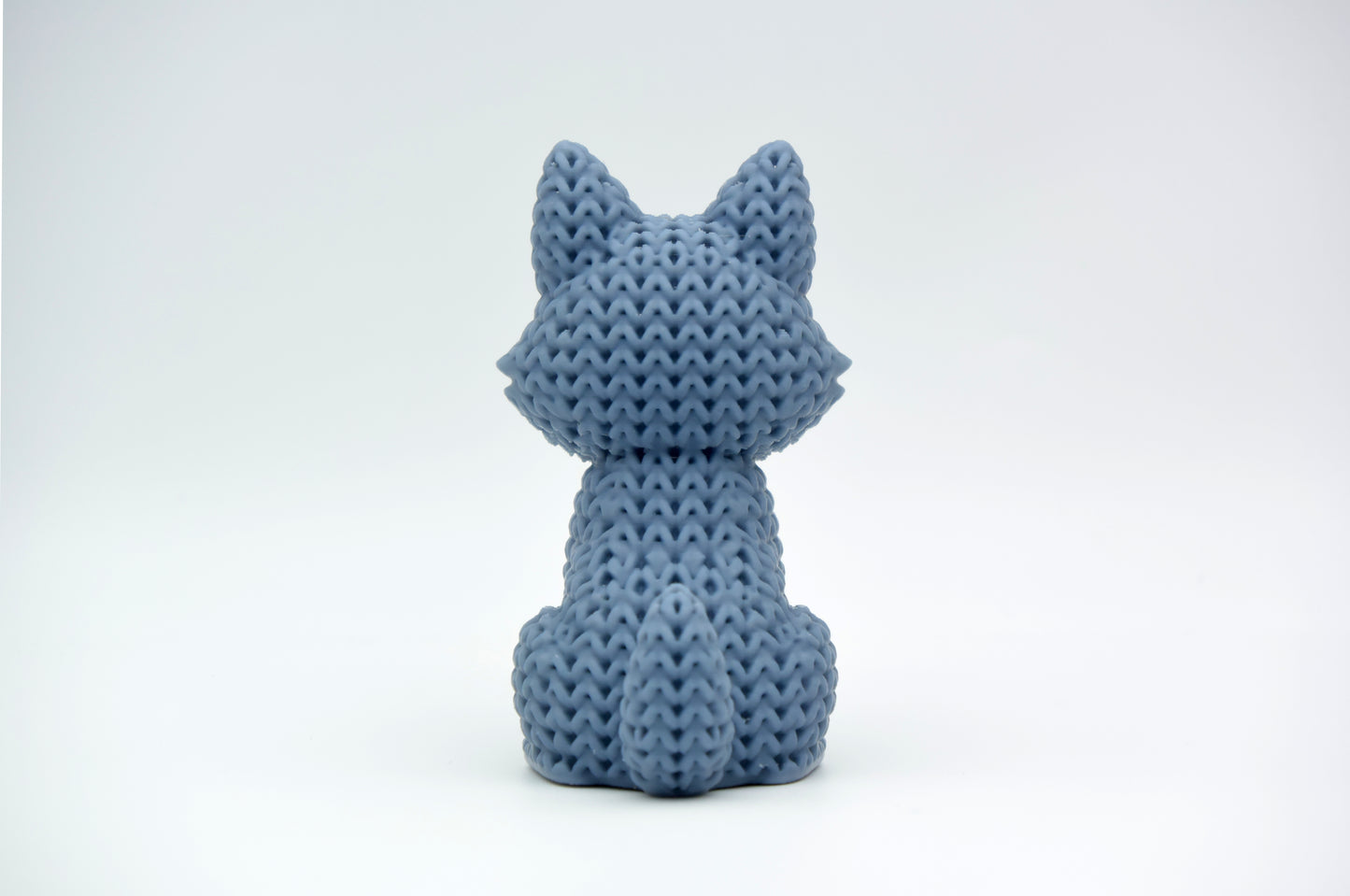 Close-up of a knitted wolf figurine showing crochet-textured surface in warm grey tones, approx 10 cm tall