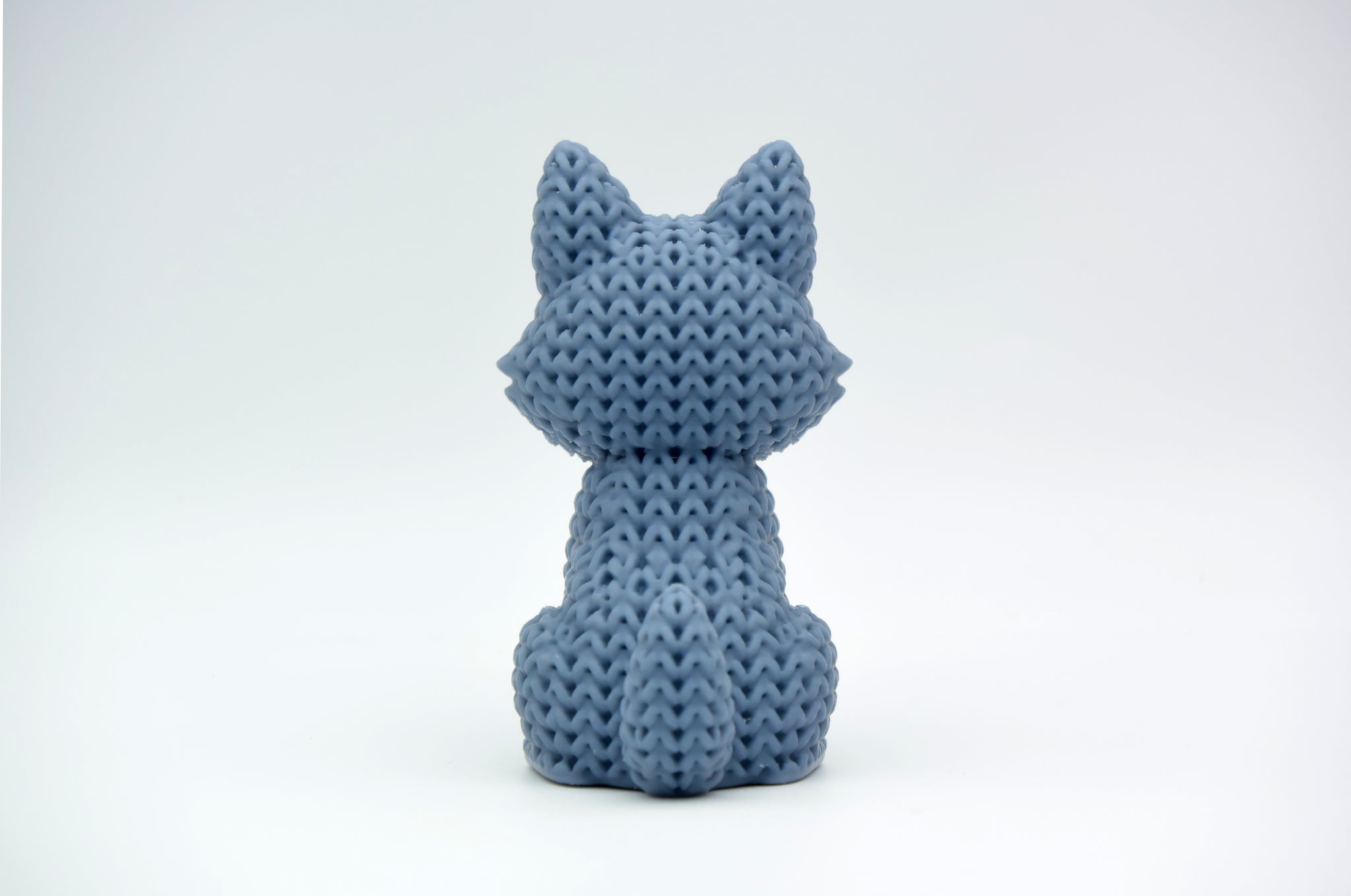 Close-up of a knitted wolf figurine showing crochet-textured surface in warm grey tones, approx 10 cm tall