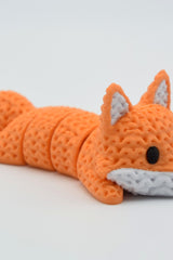 Knitted articulated fox lying on a white surface, showing its flexible segmented body and crochet-like texture