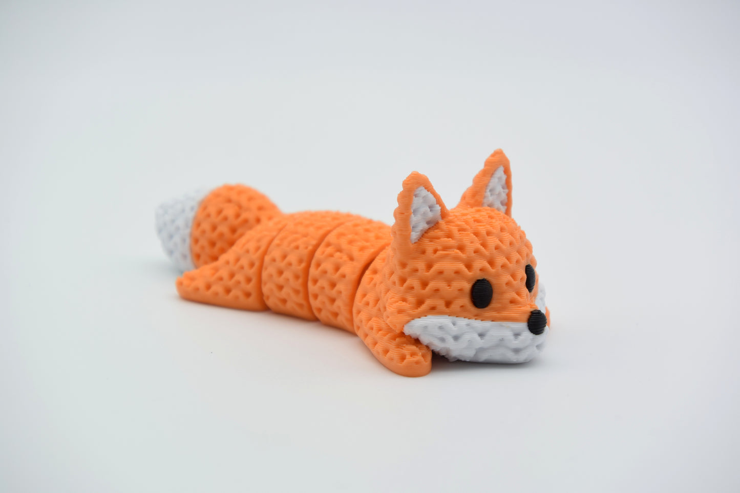 Knitted articulated fox lying on a white surface, showing its flexible segmented body and crochet-like texture