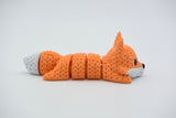 Knitted articulated fox lying on a white surface, showing its flexible segmented body and crochet-like texture