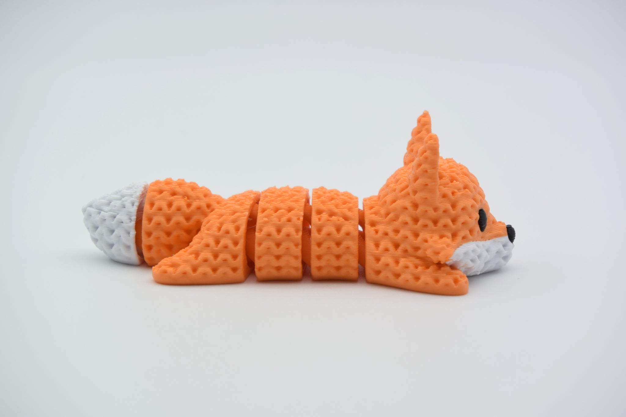 Knitted articulated fox lying on a white surface, showing its flexible segmented body and crochet-like texture
