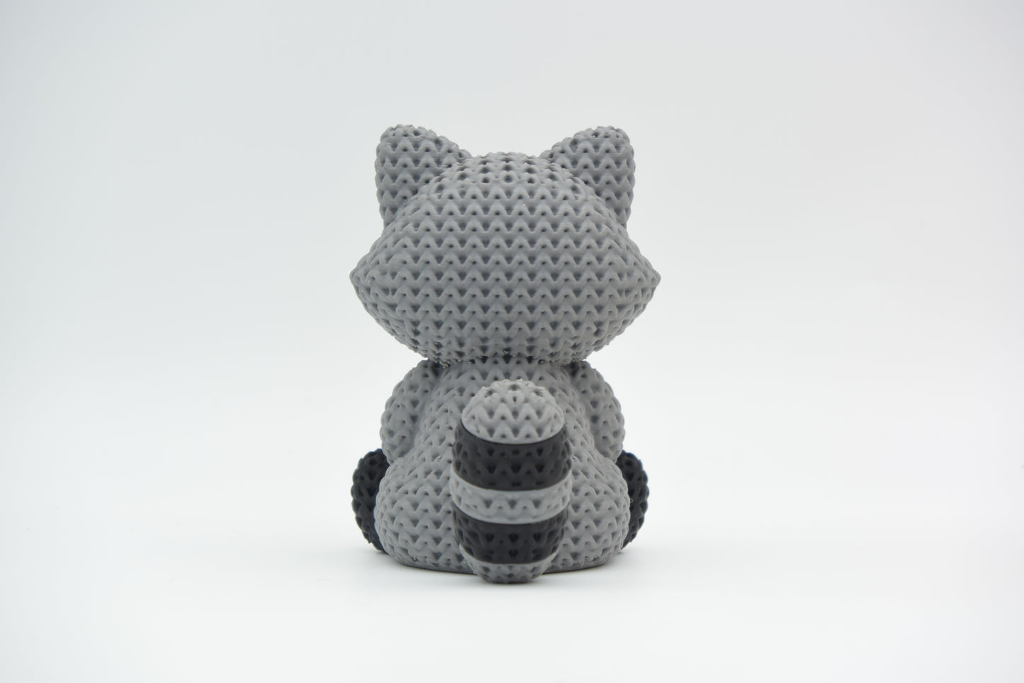 Detail shot of the crochet-style surface texture on a knitted raccoon ornament, showing the fine weave pattern