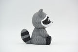 Close-up of a knitted raccoon figurine with a detailed crochet-look texture, shown against a white background