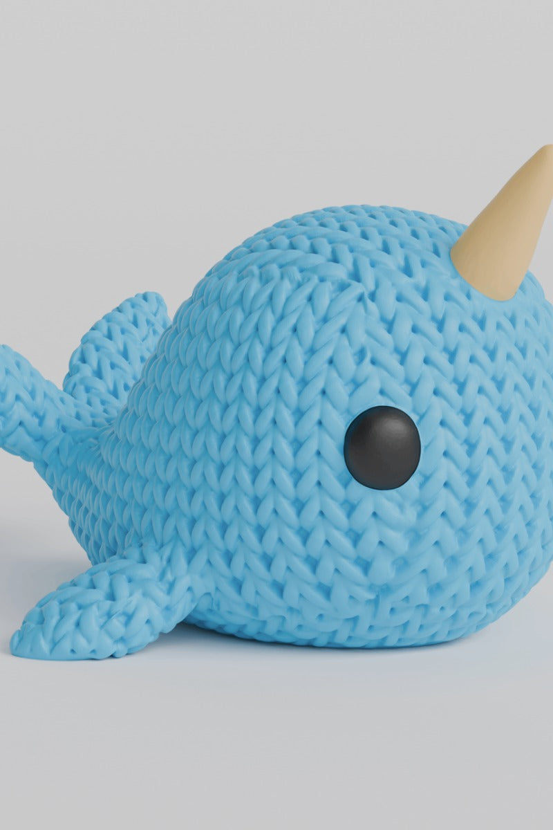 Close-up of a knitted narwhal figurine with crochet-textured surface and spiral horn, photographed on a white background