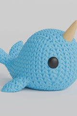 Close-up of a knitted narwhal figurine with crochet-textured surface and spiral horn, photographed on a white background