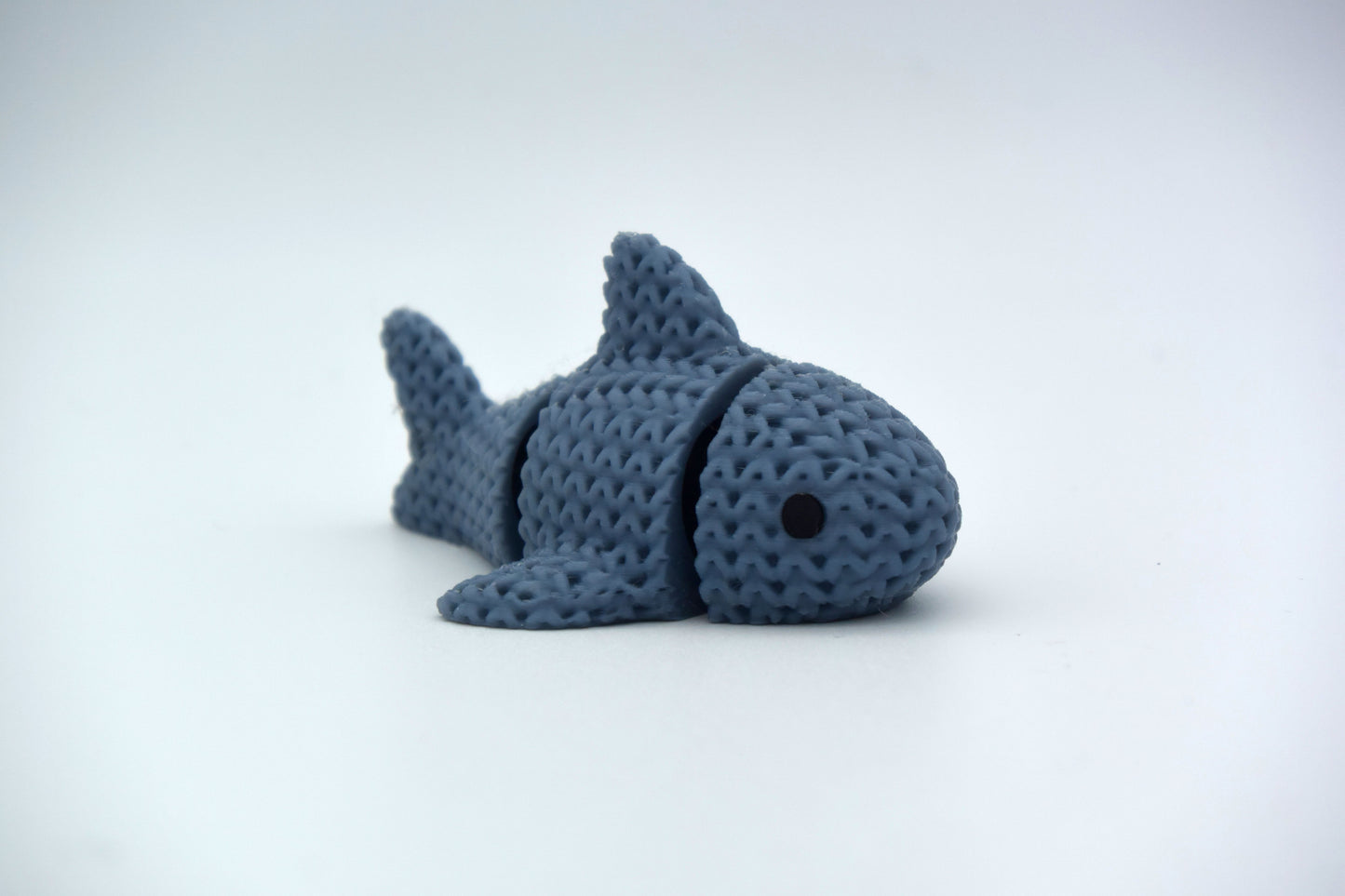 Close-up of a knitted articulated shark with a soft crochet texture, shown on a white surface