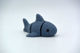 Close-up of a knitted articulated shark with a soft crochet texture, shown on a white surface