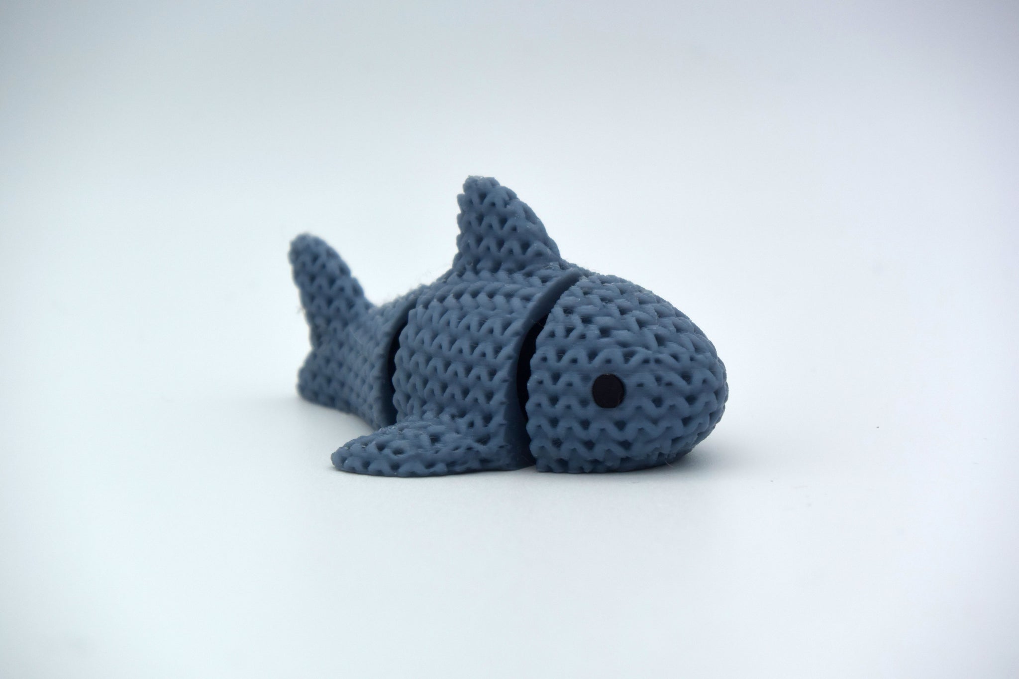 Close-up of a knitted articulated shark with a soft crochet texture, shown on a white surface