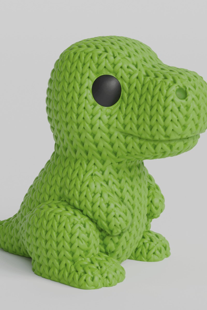 Close-up of a knitted T-Rex dinosaur figurine with a soft crochet-look surface texture, shown in sage green
