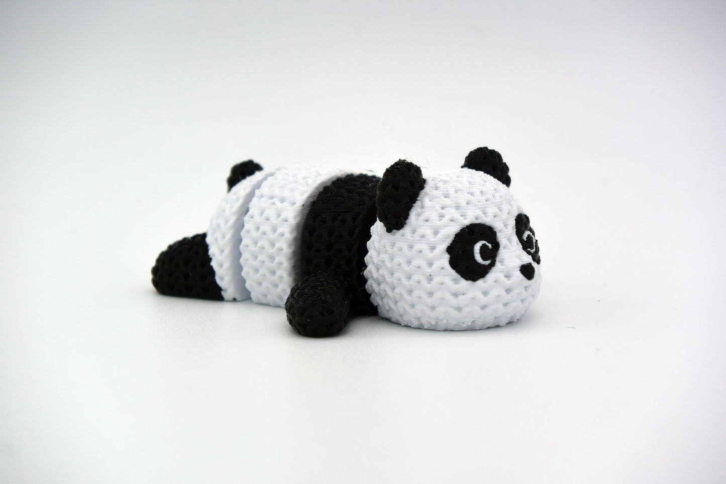 Small knitted panda posed on a wooden shelf next to books and a plant in a Scandinavian interior