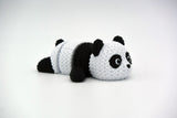 Small knitted panda posed on a wooden shelf next to books and a plant in a Scandinavian interior