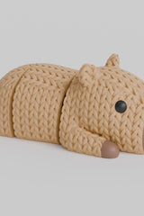 Close-up of a knitted capybara figurine with a soft crochet-like texture and articulated legs, shown on a white surface