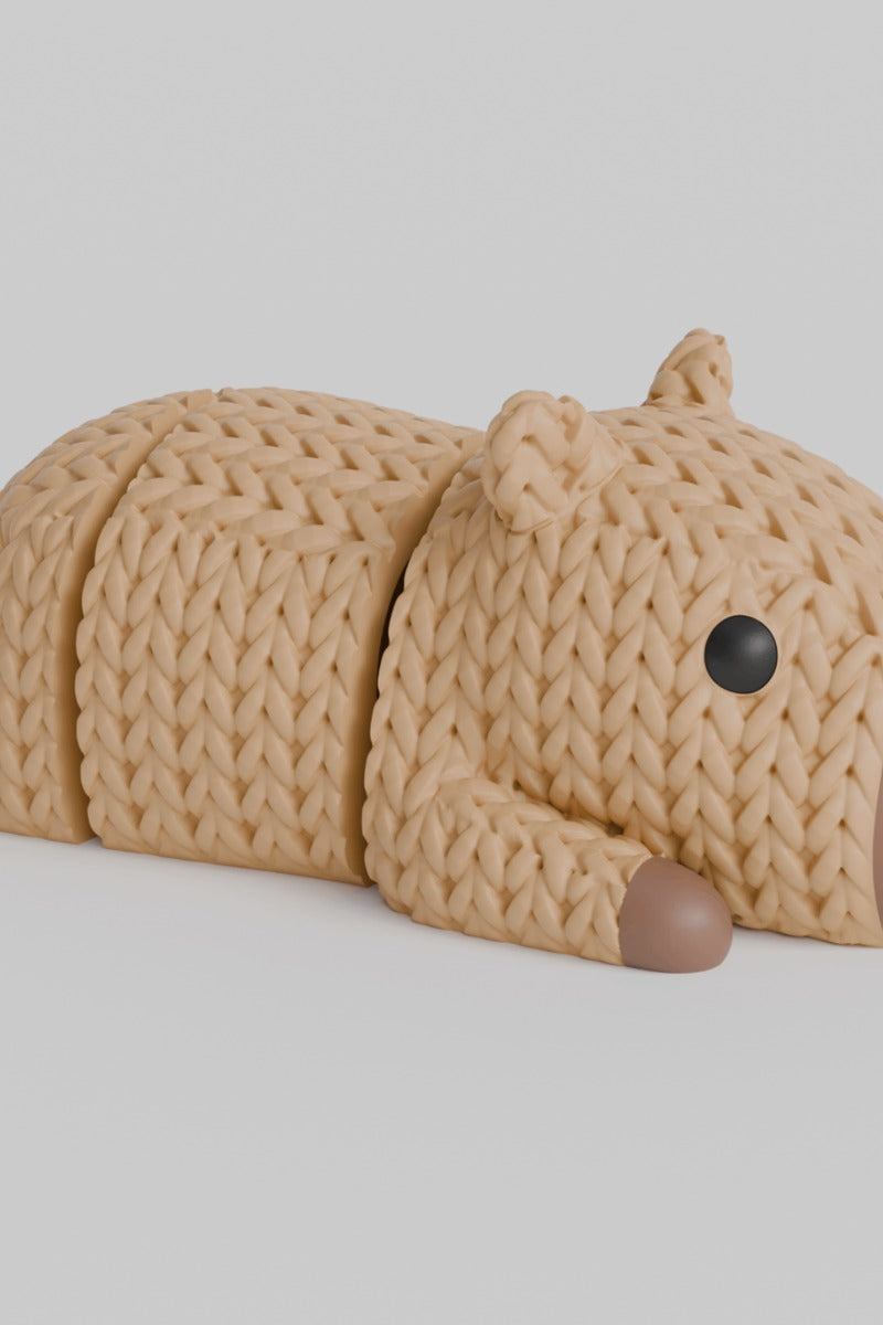 Close-up of a knitted capybara figurine with a soft crochet-like texture and articulated legs, shown on a white surface