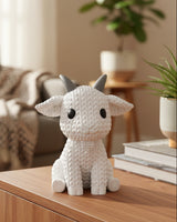 Close-up of a knitted goat decoration with a soft crochet-look texture, shown on a white surface