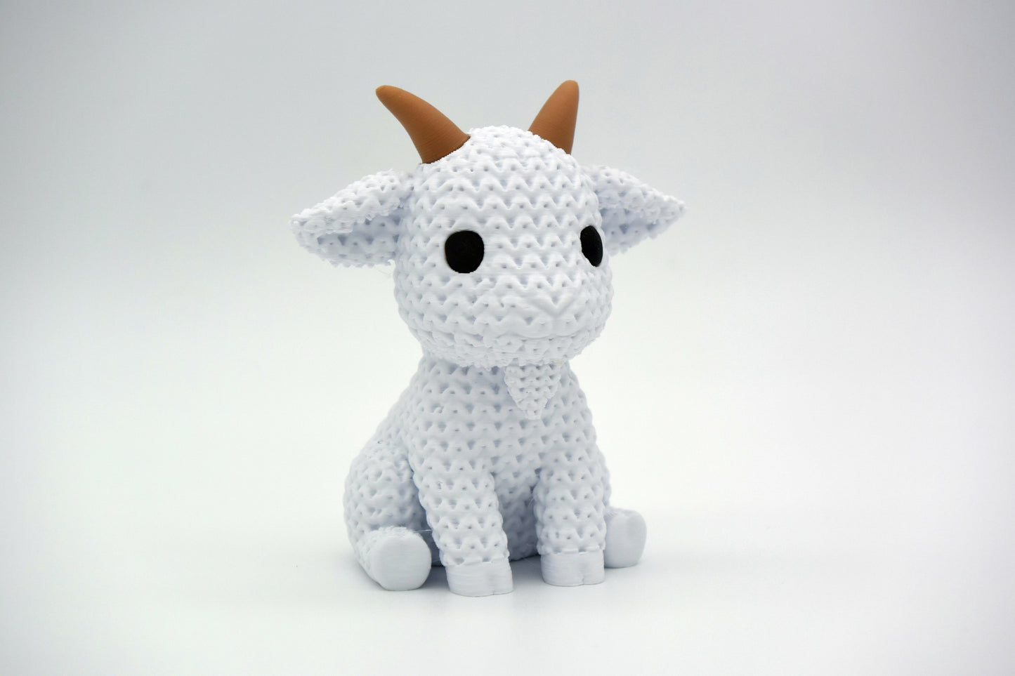 Knitted goat decoration styled on a wooden shelf beside a small plant and neutral ceramic pot