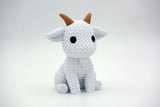 Knitted goat decoration styled on a wooden shelf beside a small plant and neutral ceramic pot