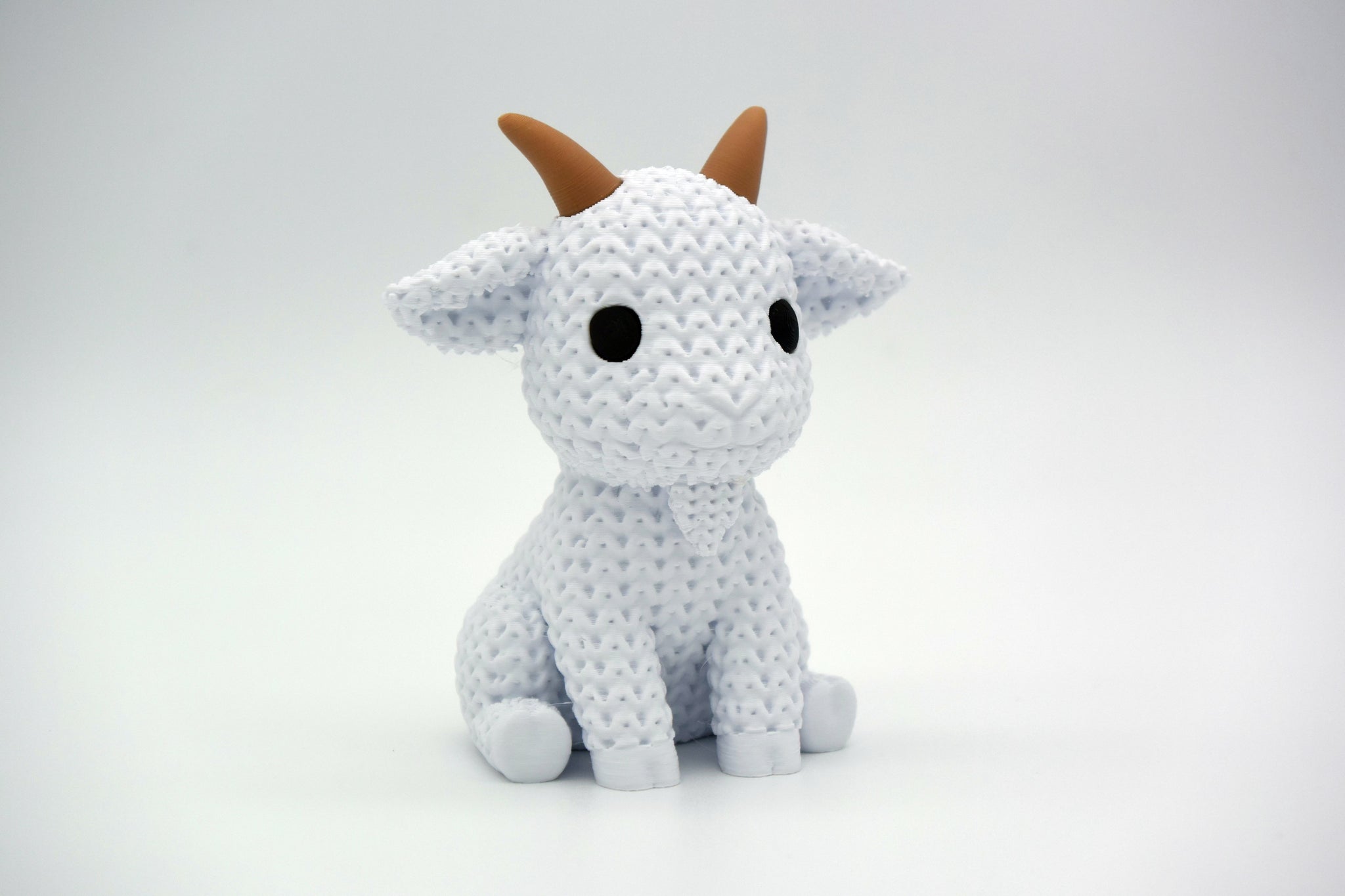Knitted goat decoration styled on a wooden shelf beside a small plant and neutral ceramic pot
