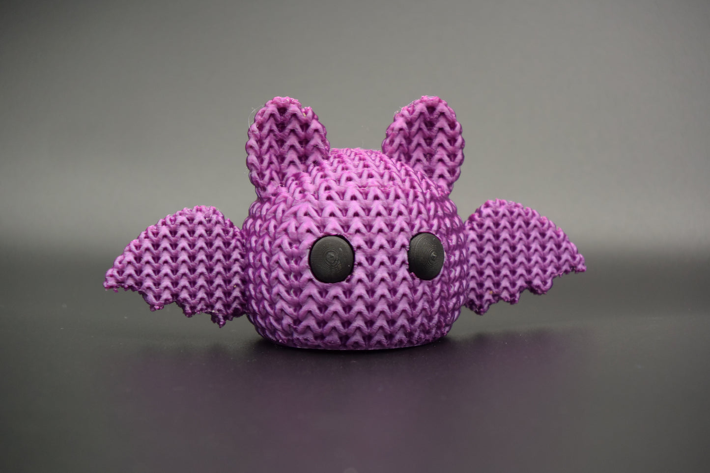 Knitted Halloween bat decoration styled on a wooden shelf beside autumn candles and dried leaves in a Scandinavian home
