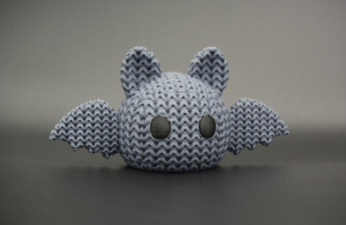 Close-up of a knitted Halloween bat decoration with a soft crochet-look texture and small eyes, shot on a light surface