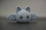 Close-up of a knitted Halloween bat decoration with a soft crochet-look texture and small eyes, shot on a light surface