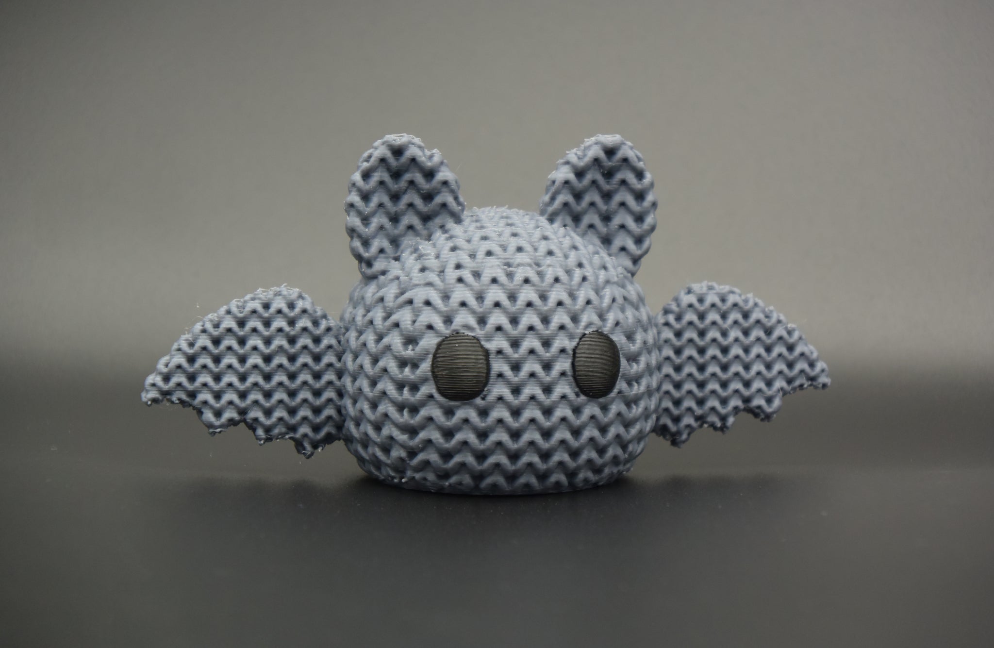 Close-up of a knitted Halloween bat decoration with a soft crochet-look texture and small eyes, shot on a light surface