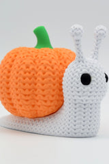 Close-up of a knitted pumpkin snail decoration with soft crochet texture and orange ribbed shell, on white background