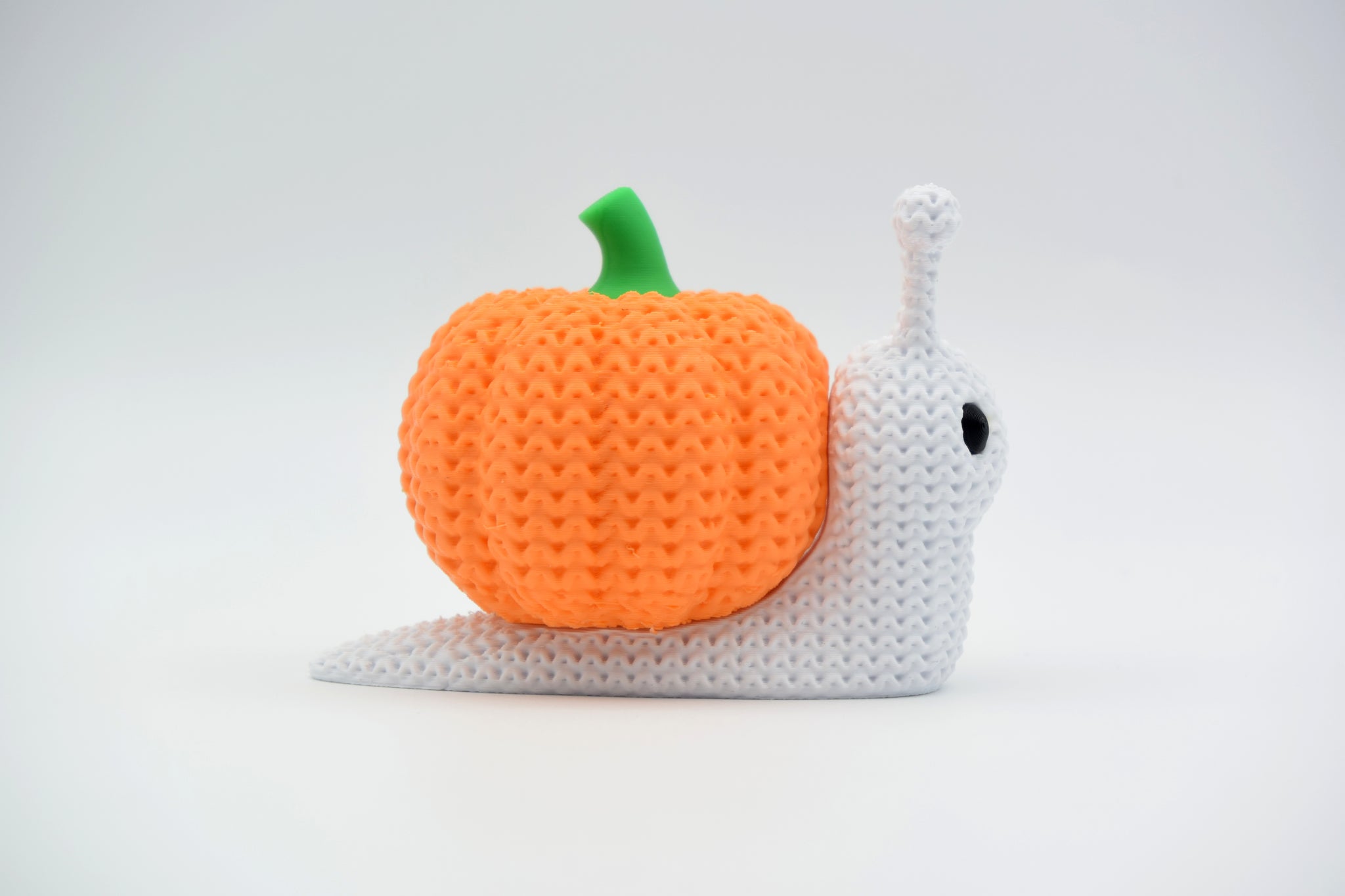 Knitted pumpkin snail Halloween decoration styled on a wooden shelf with dried autumn leaves and small candles