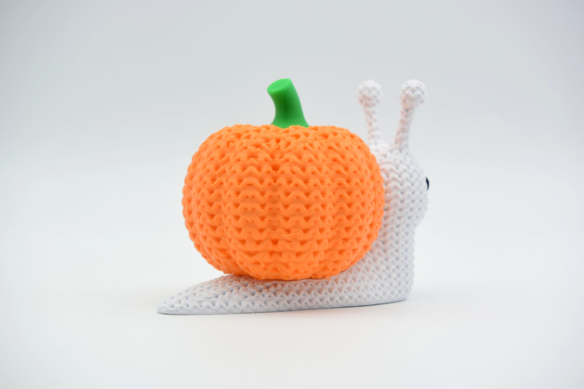 Texture detail of the crochet-look surface on a knitted pumpkin snail, showing the woven ridge pattern of the shell