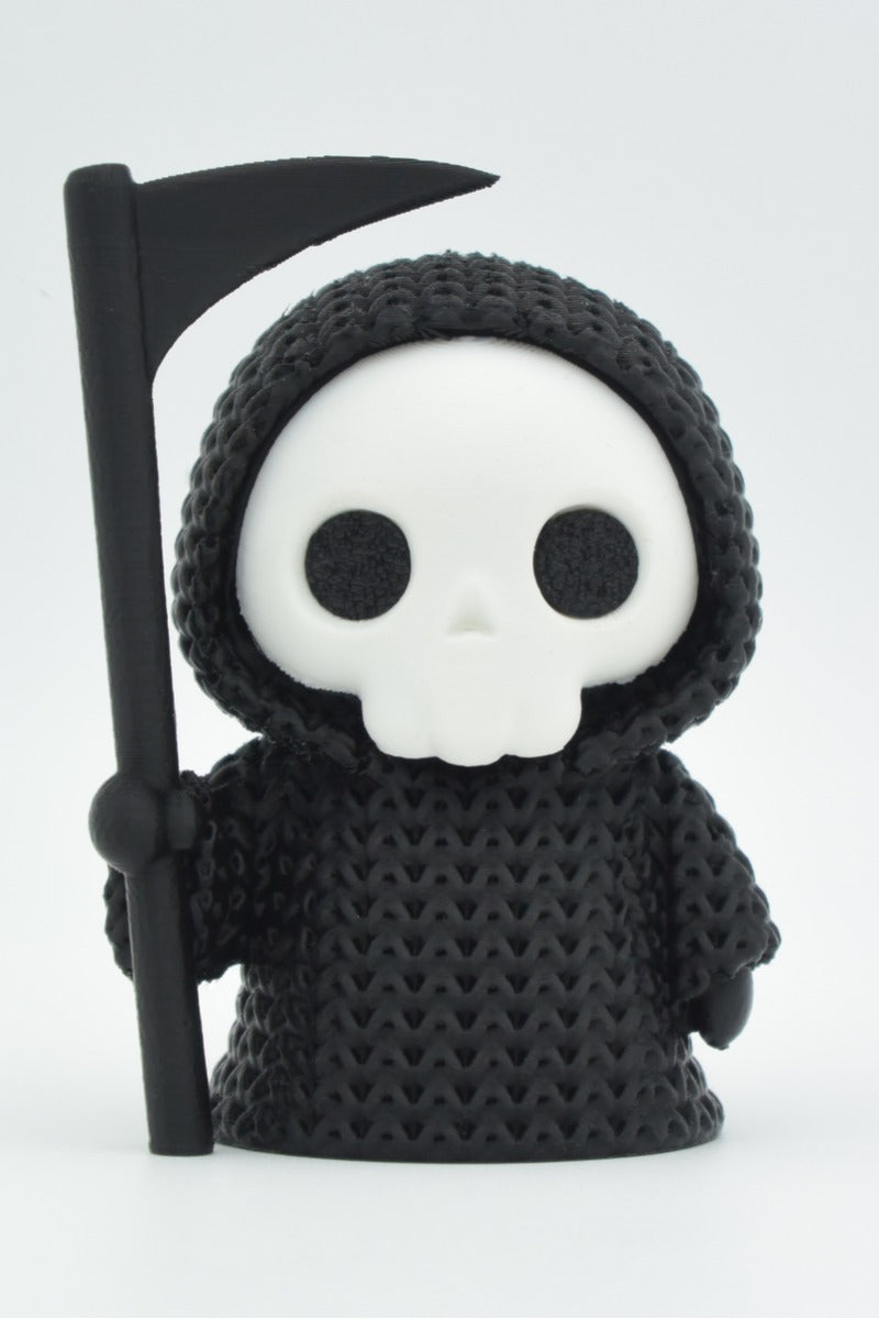Close-up of a knitted grim reaper decoration with hooded cloak and scythe, soft crochet-like texture