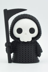 Close-up of a knitted grim reaper decoration with hooded cloak and scythe, soft crochet-like texture