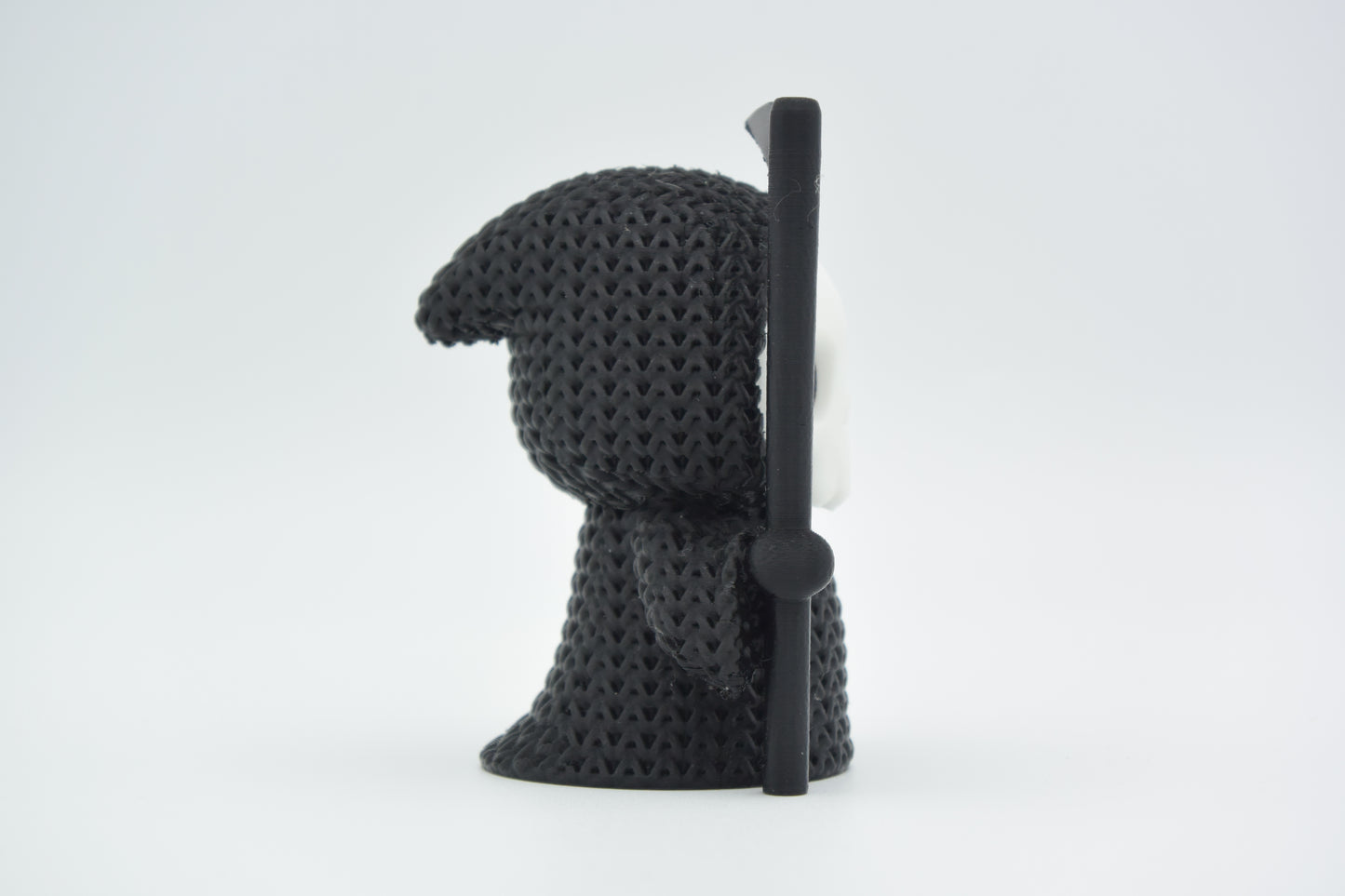 Small knitted grim reaper Halloween decoration styled on a dark wooden shelf beside autumn foliage