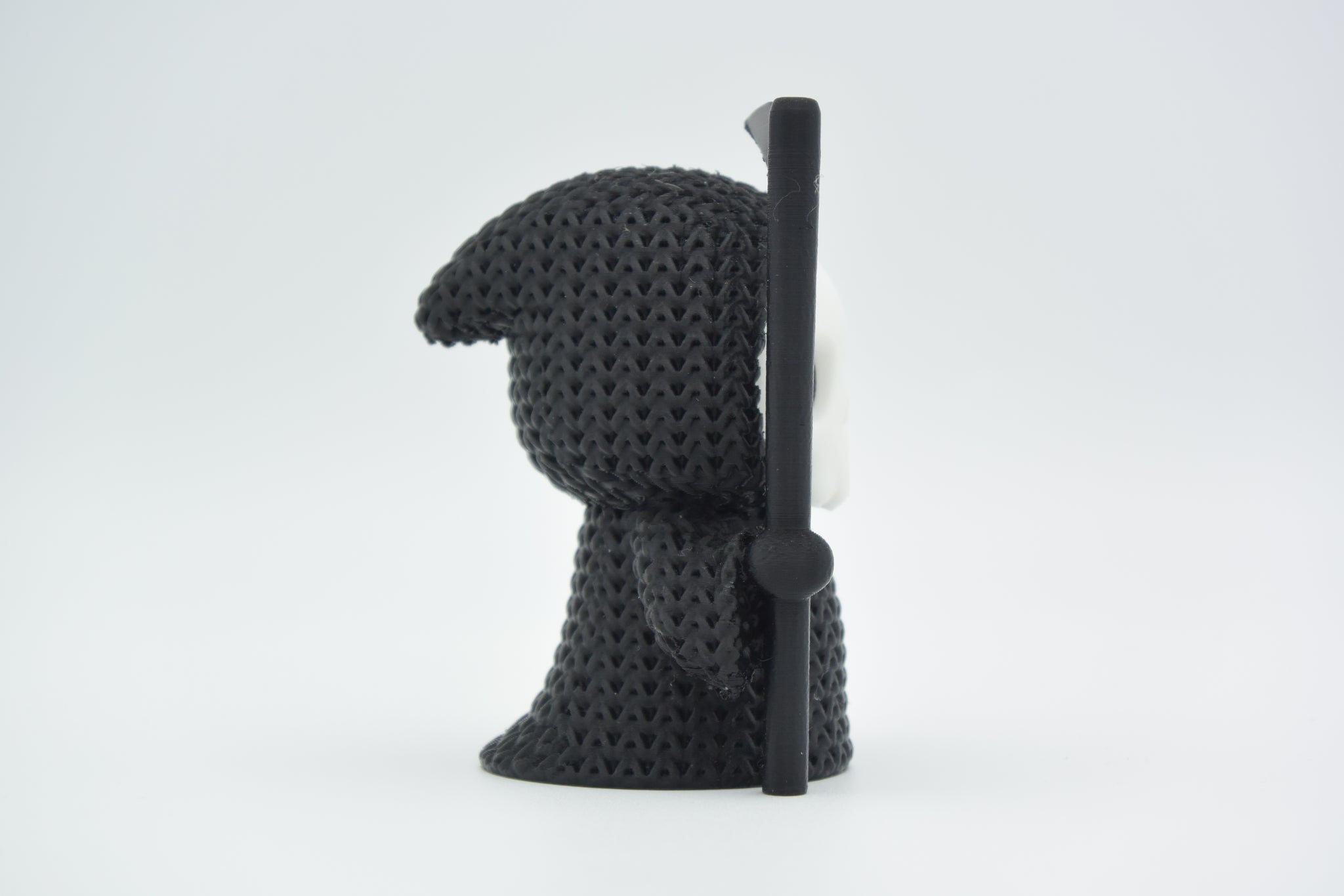 Small knitted grim reaper Halloween decoration styled on a dark wooden shelf beside autumn foliage