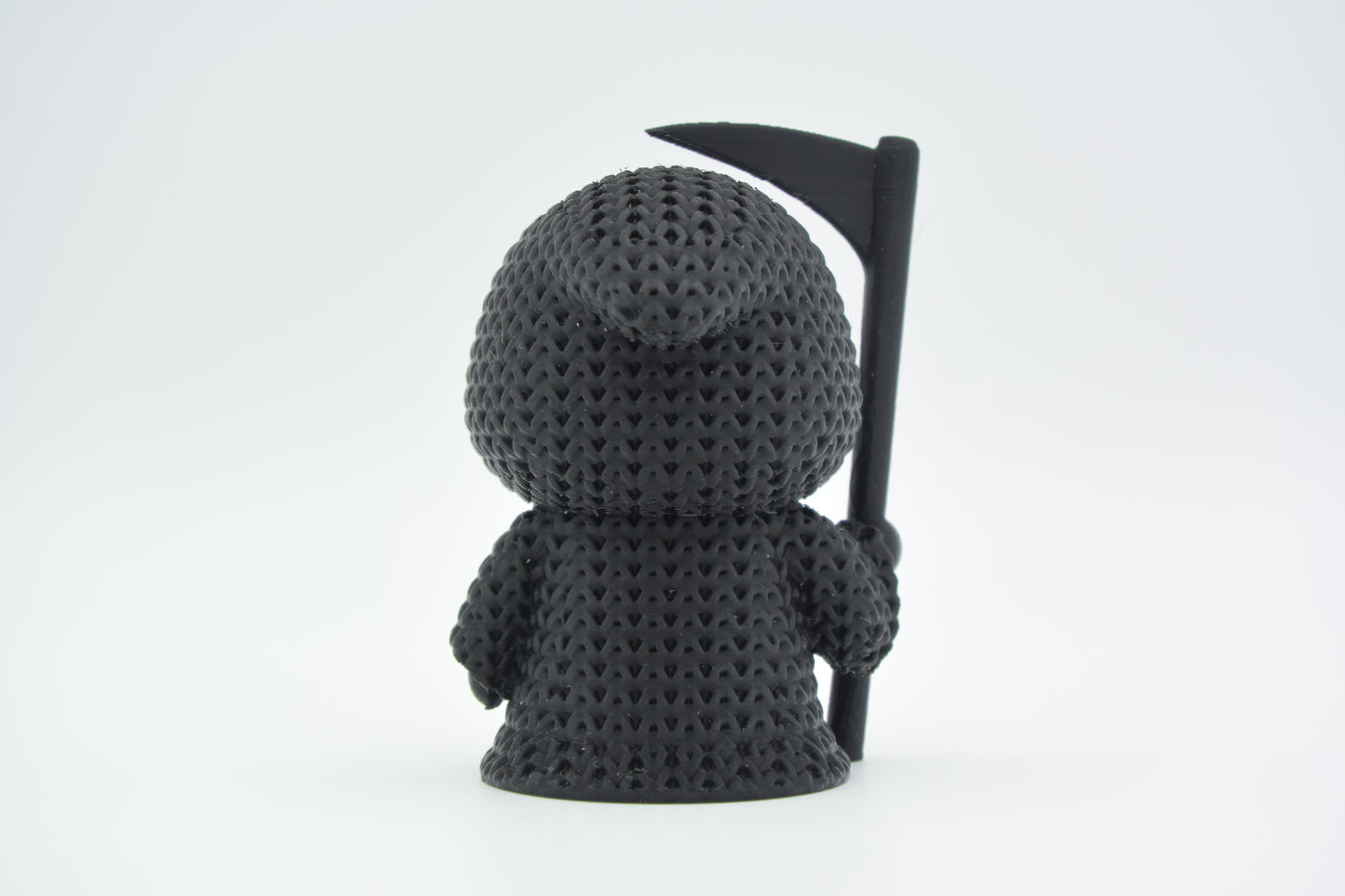 Detail shot of the looping yarn texture on a knitted grim reaper figure, showing the woven surface pattern