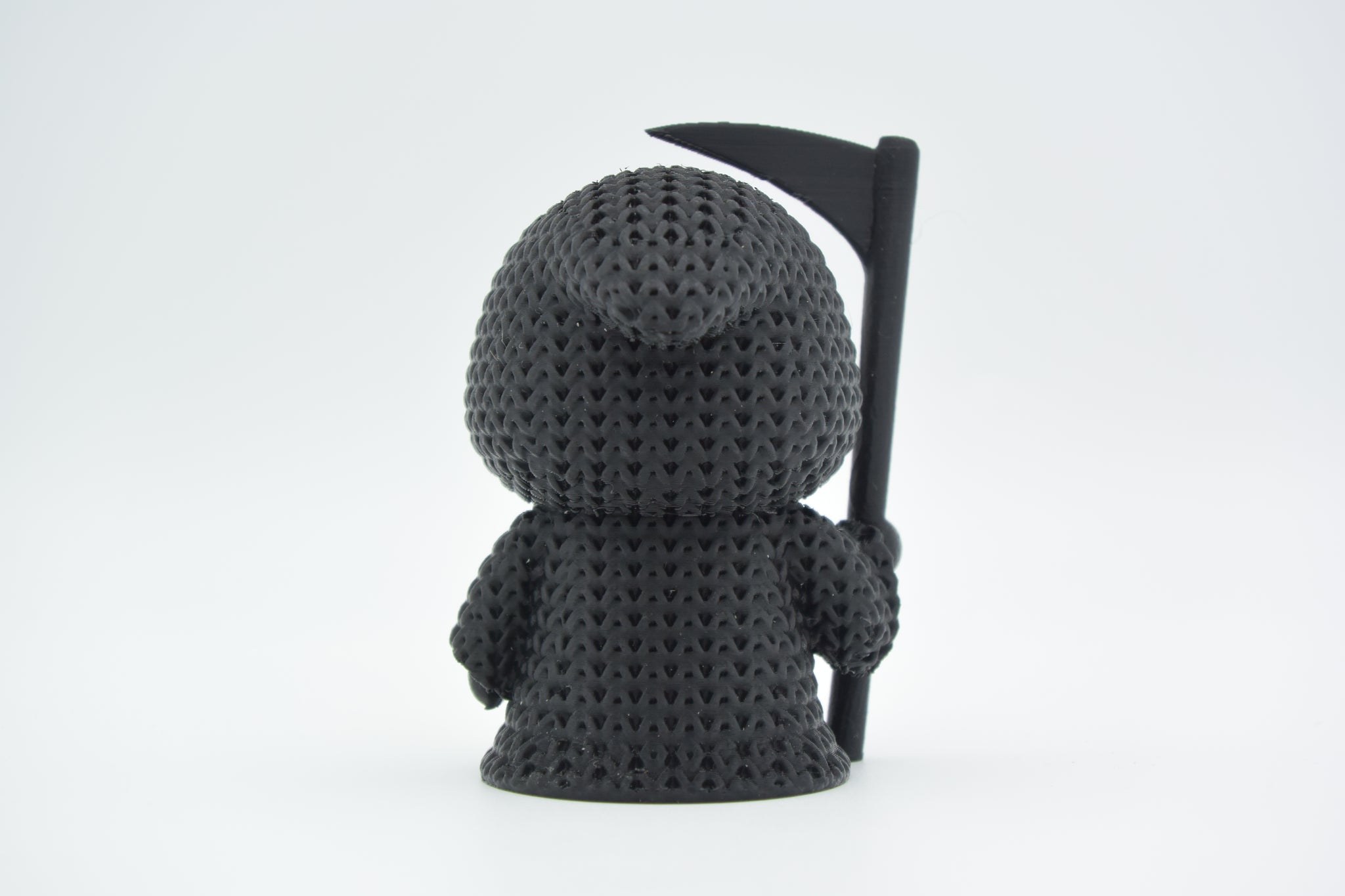 Detail shot of the looping yarn texture on a knitted grim reaper figure, showing the woven surface pattern