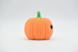 Crochet pumpkin decoration placed on a wooden shelf beside autumn leaves and a small candle in a cosy home setting