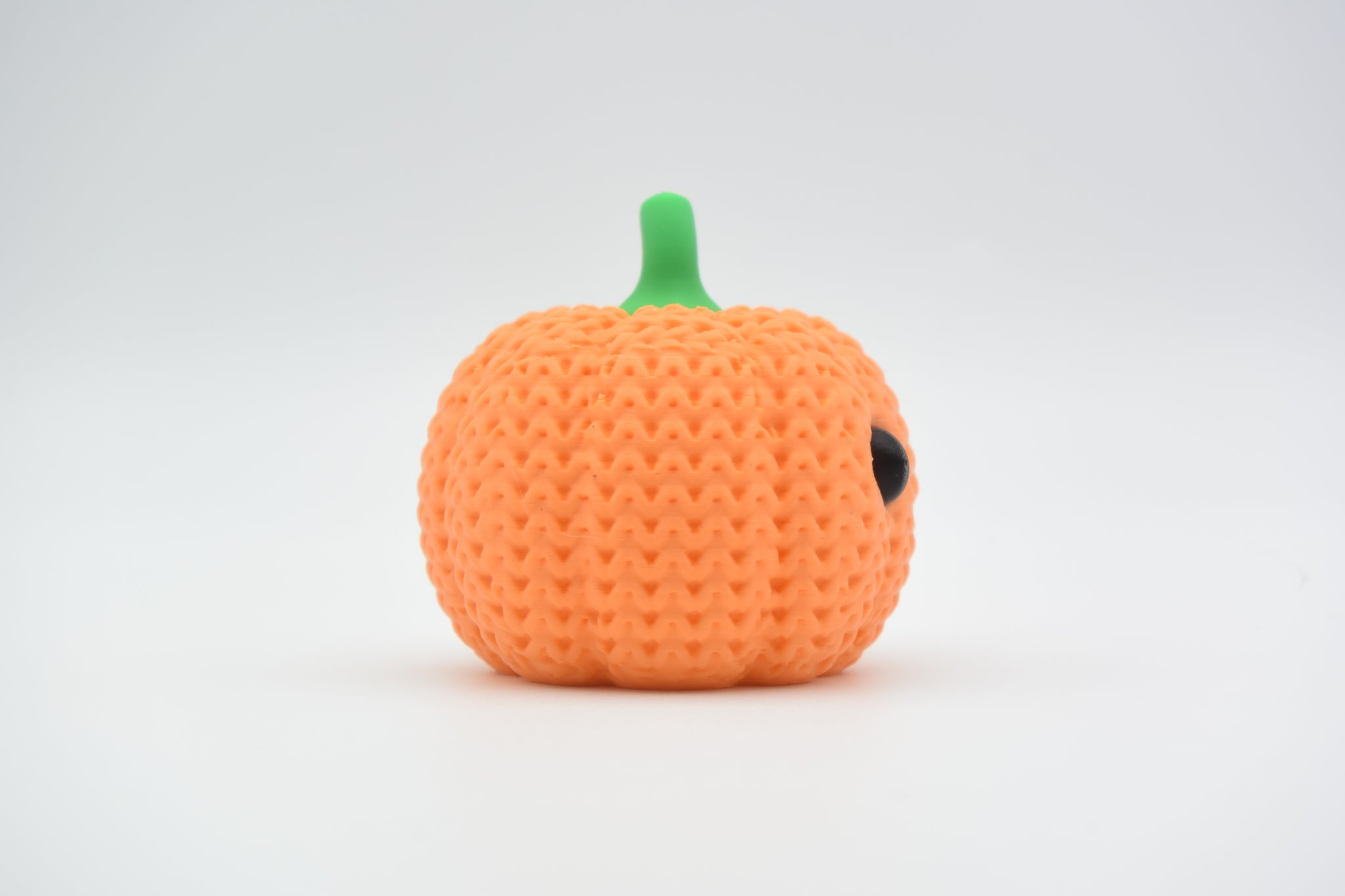 Crochet pumpkin decoration placed on a wooden shelf beside autumn leaves and a small candle in a cosy home setting