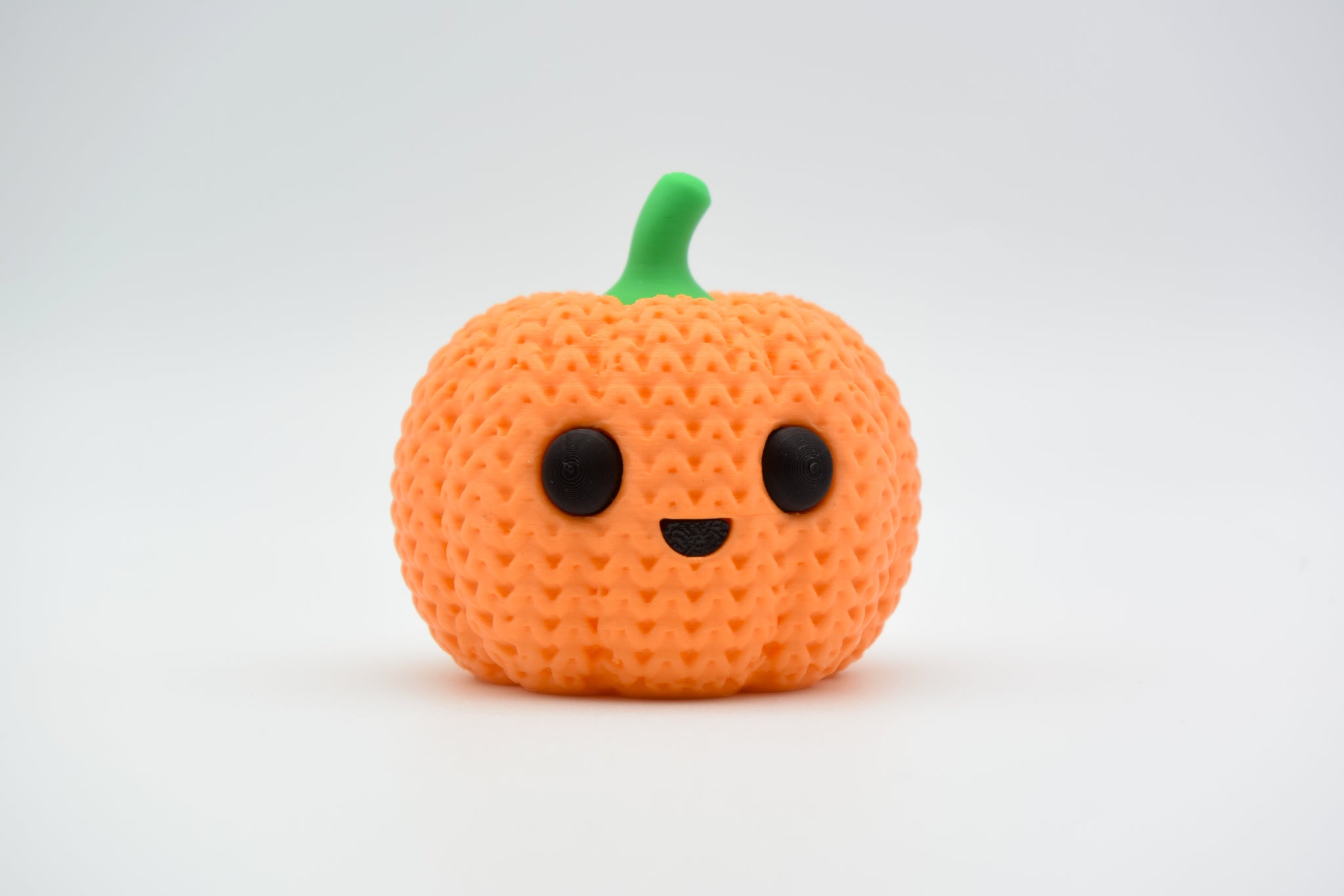Close-up of a crochet pumpkin decoration with ribbed knitted texture and small stem, shot on white surface