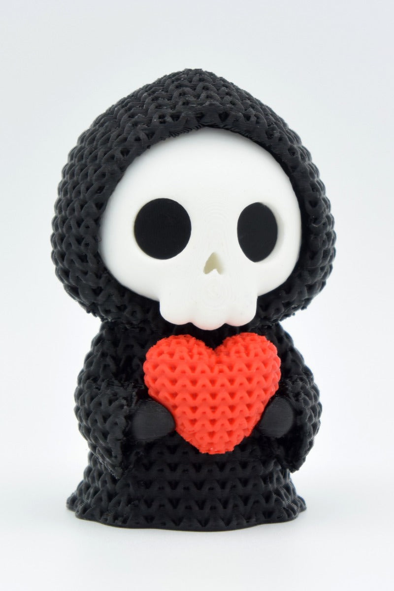 Close-up of a crochet grim reaper decoration holding a small heart, soft knitted texture visible across the hooded figure