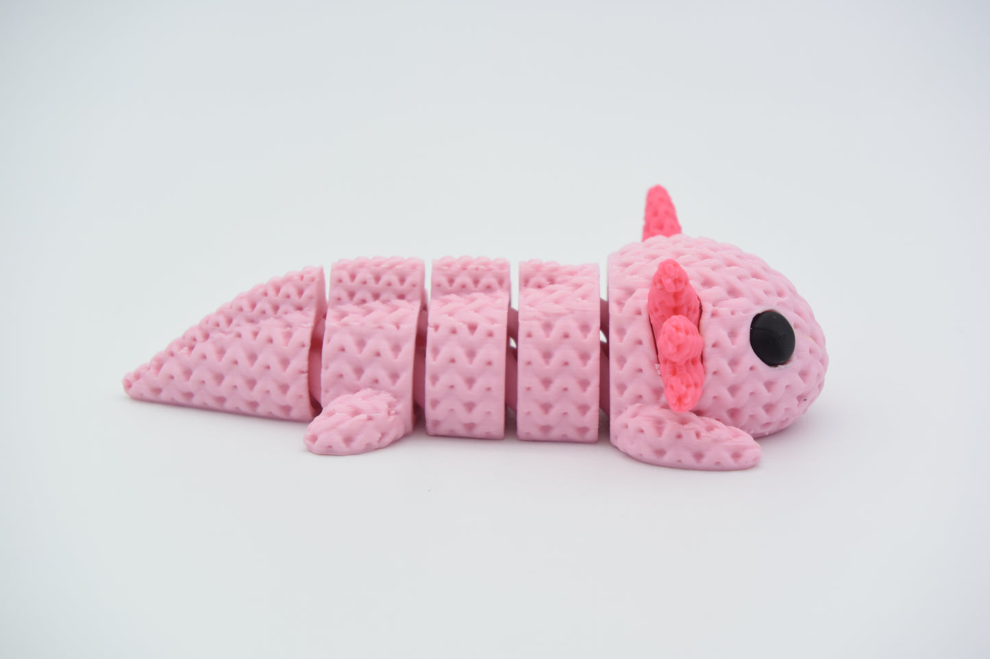 Knitted axolotl flexi figure resting on a wooden shelf beside a small plant in a calm home setting
