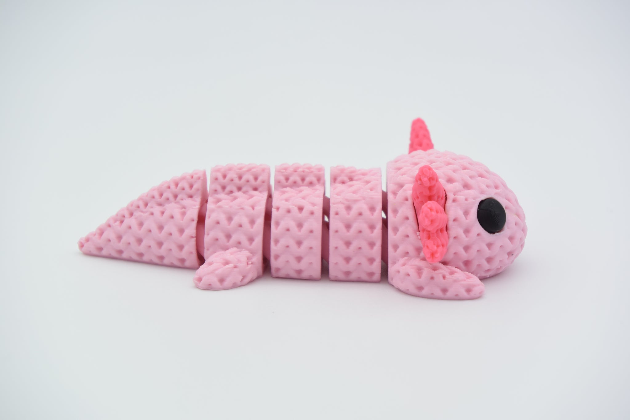 Knitted axolotl flexi figure resting on a wooden shelf beside a small plant in a calm home setting