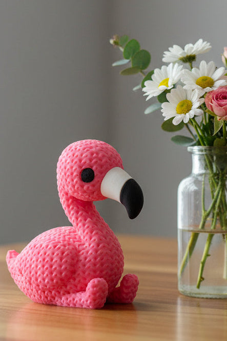 Close-up of a pink knitted flamingo figurine with a soft crochet-look surface texture, standing upright