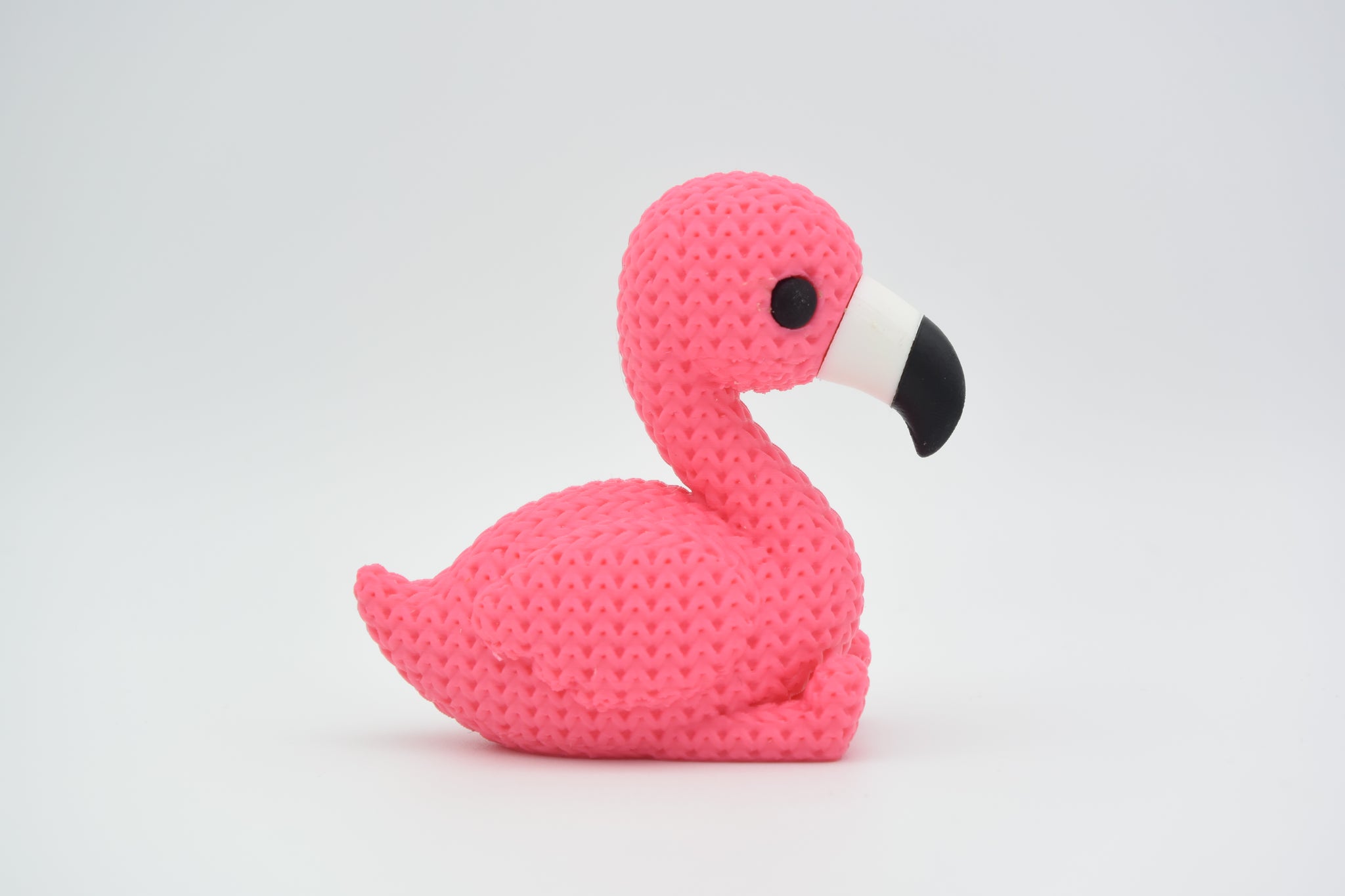 Knitted flamingo decorative figurine styled on a wooden shelf beside a small plant and neutral home decor