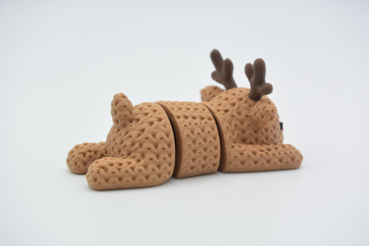 Knitted reindeer decoration posed on a wooden shelf beside pine branches and a white candle