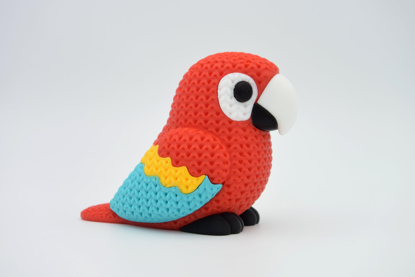 Close-up of a knitted scarlet macaw parrot figurine with textured red, blue and yellow surface detail
