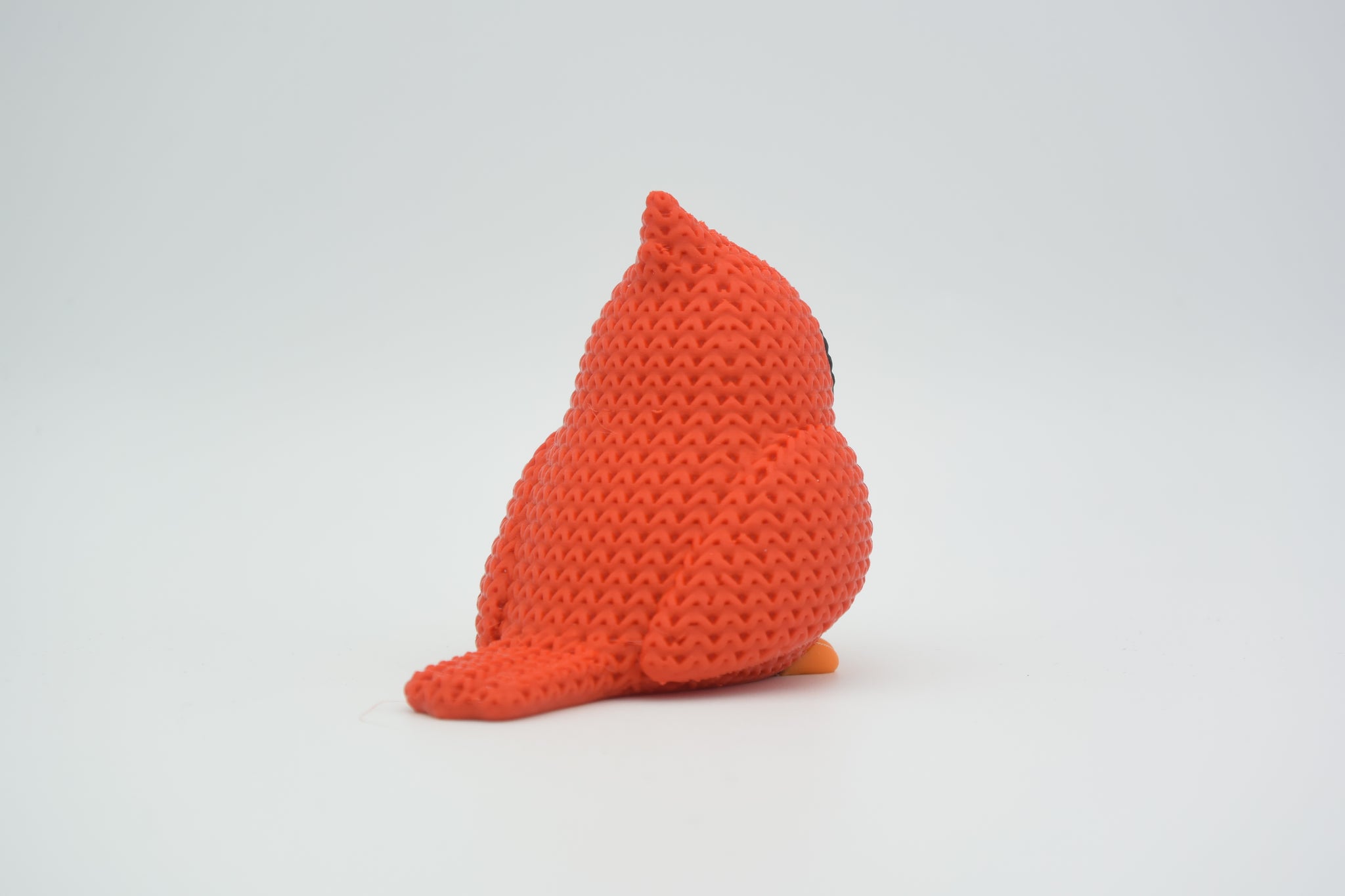 Small red knitted cardinal bird decoration resting on a wooden shelf beside dried botanicals